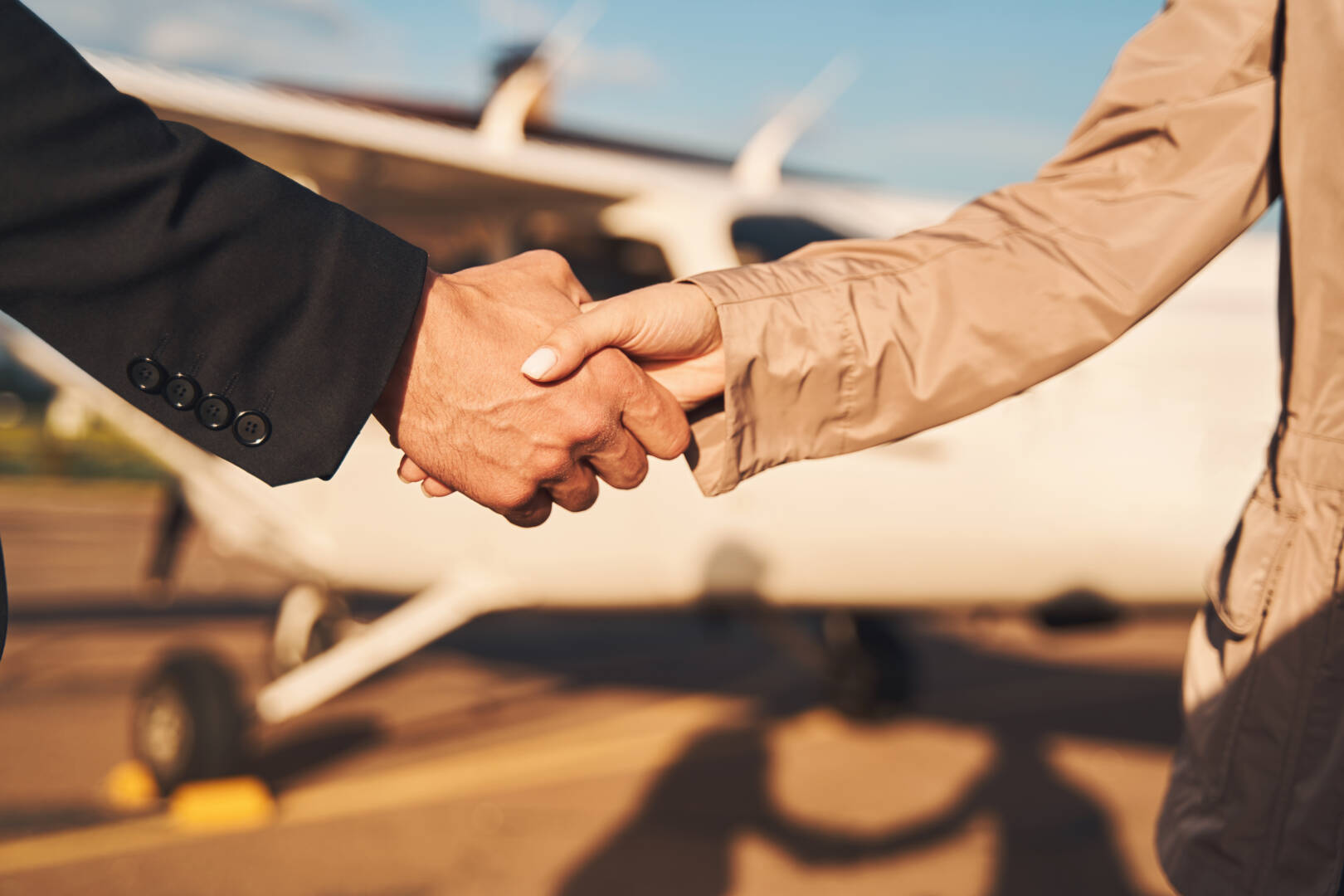 Close up of young man shaking woman hand while making successful deal on sunny day at airfield