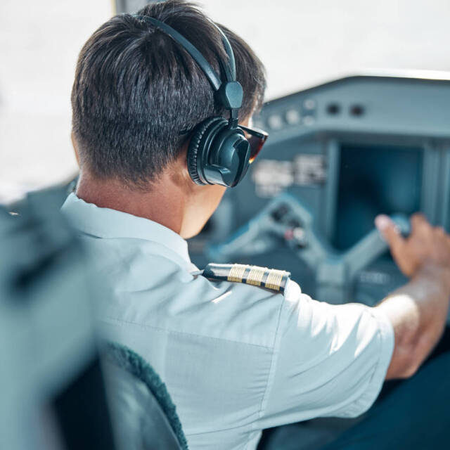 Male professional in uniform and headphones is holding rudder at control while driving jet at work